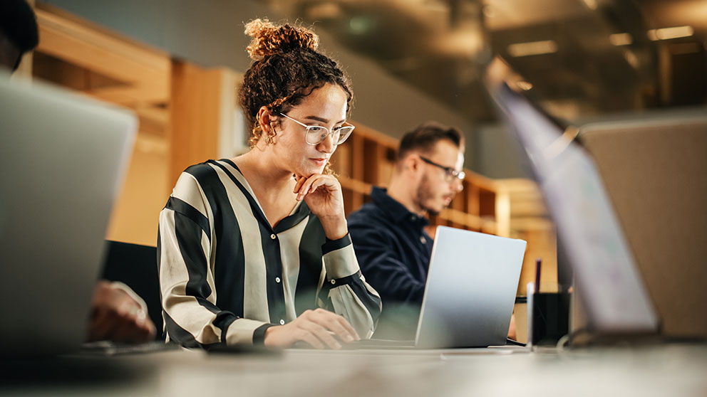 Frau lernt und arbeitet konzentriert am Laptop, im Hintergrund eine weitere Person
