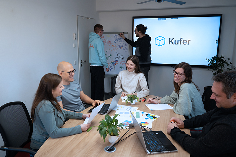Team bei einem Workshop, eine Person schreibt an einem Whiteboard, weitere sitzen am Tisch