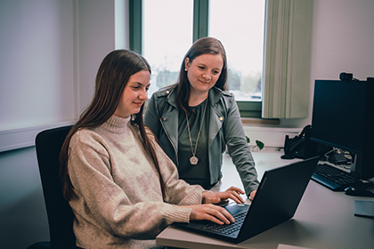 Zwei junge Frauen sitzen im Büro und arbeiten zusammen an einem Laptop